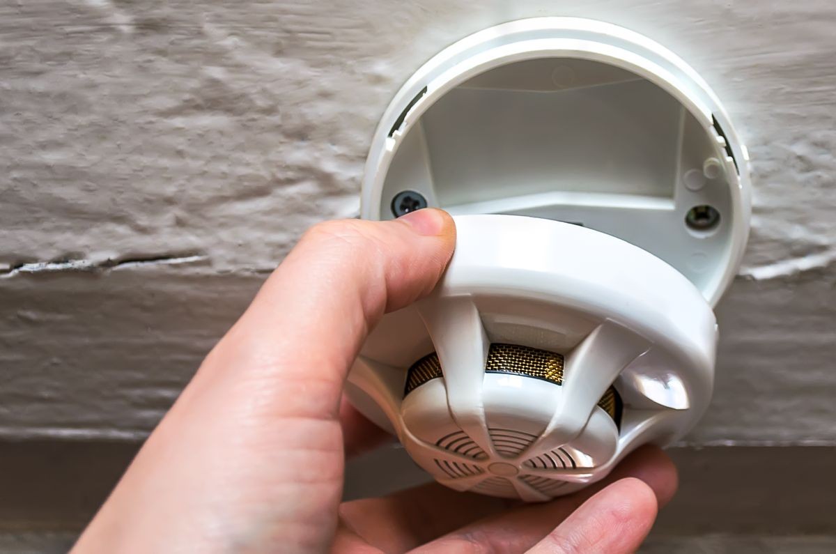 Smoke detector. Photo of a male hand taking a home smoke detector with a white ceiling background.